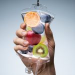 Human Hand Holding Saline Bag With Fruit Slices Over Grey Background