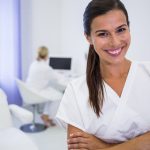 Portrait of smiling dentist standing with arms crossed at clinic