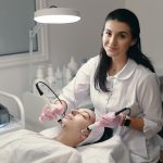 Model with closed eyes and hand's of doctor. Rejuvenating facial treatment. Model getting lifting therapy massage in a beauty SPA salon. Cosmetological clinic, procedure.